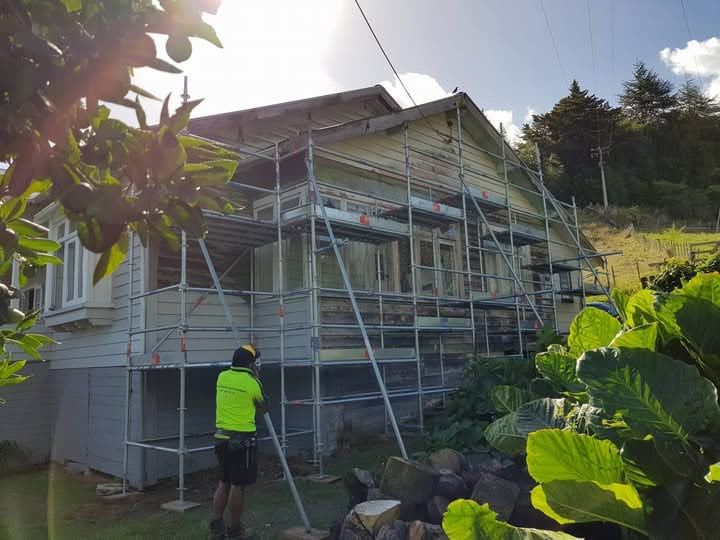 Scaffolding erected along a weatherboard house with a painter working from the deck