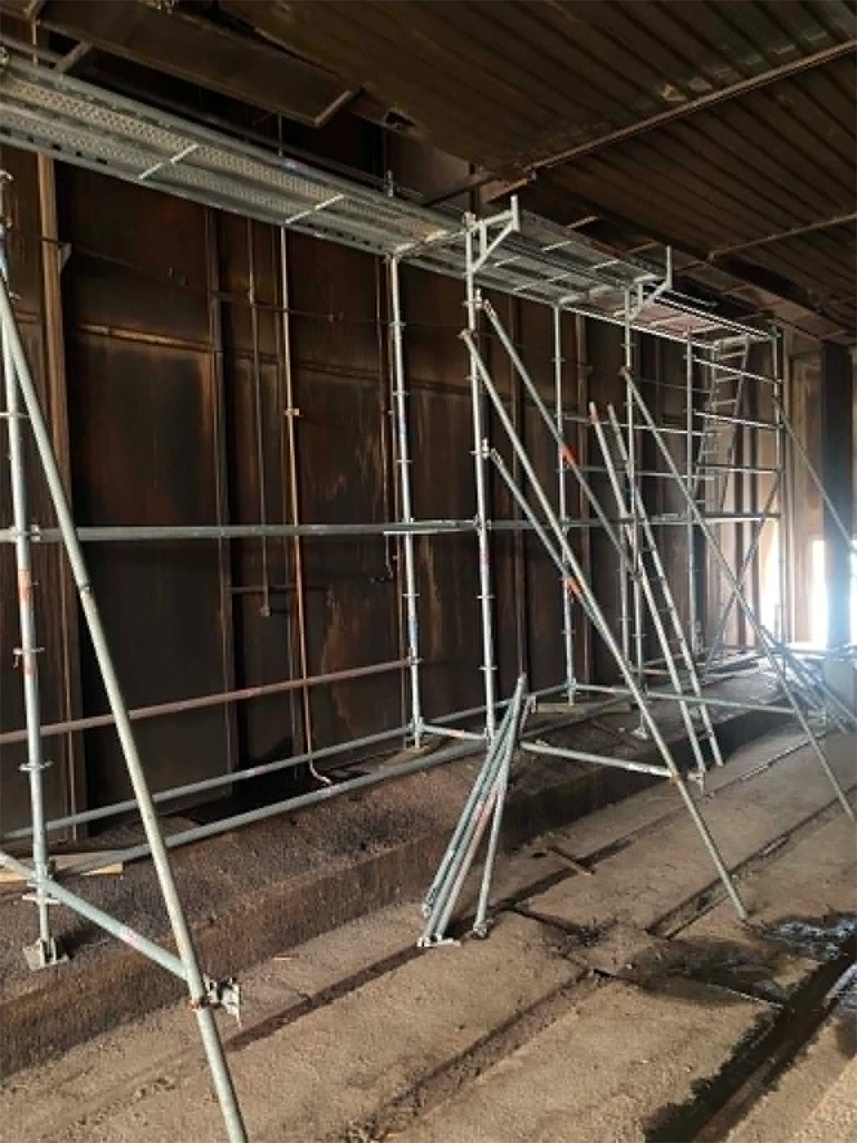 Interior scaffolding and propping set up against a timber-lined wall inside a building