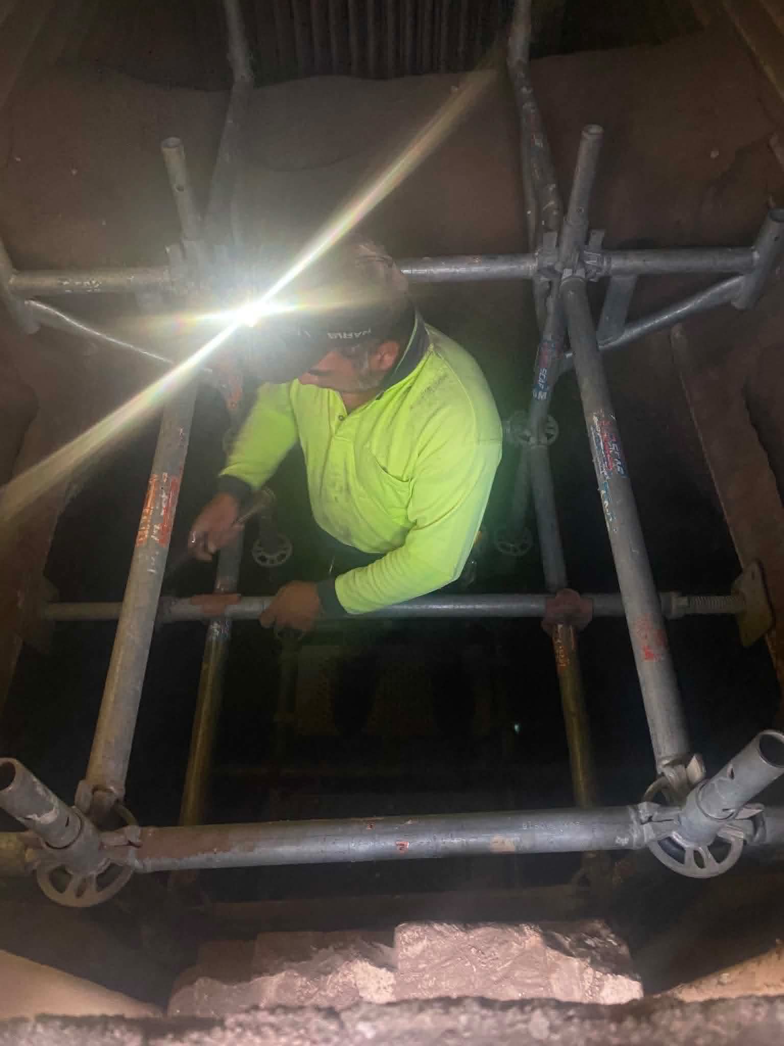 A scaffolder working by headlamp inside a dark brick shaft