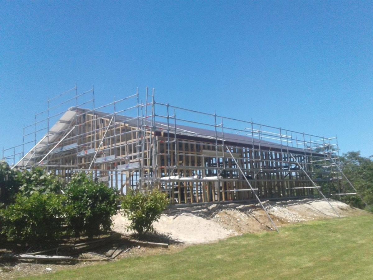 A large shed under construction with scaffolding and staging around the framing and roofline