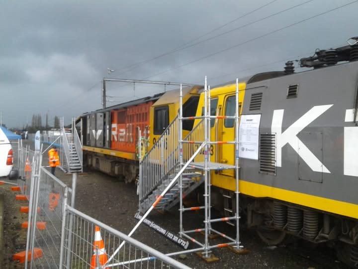 A scaffold stair tower with handrails set up alongside a locomotive in a rail yard